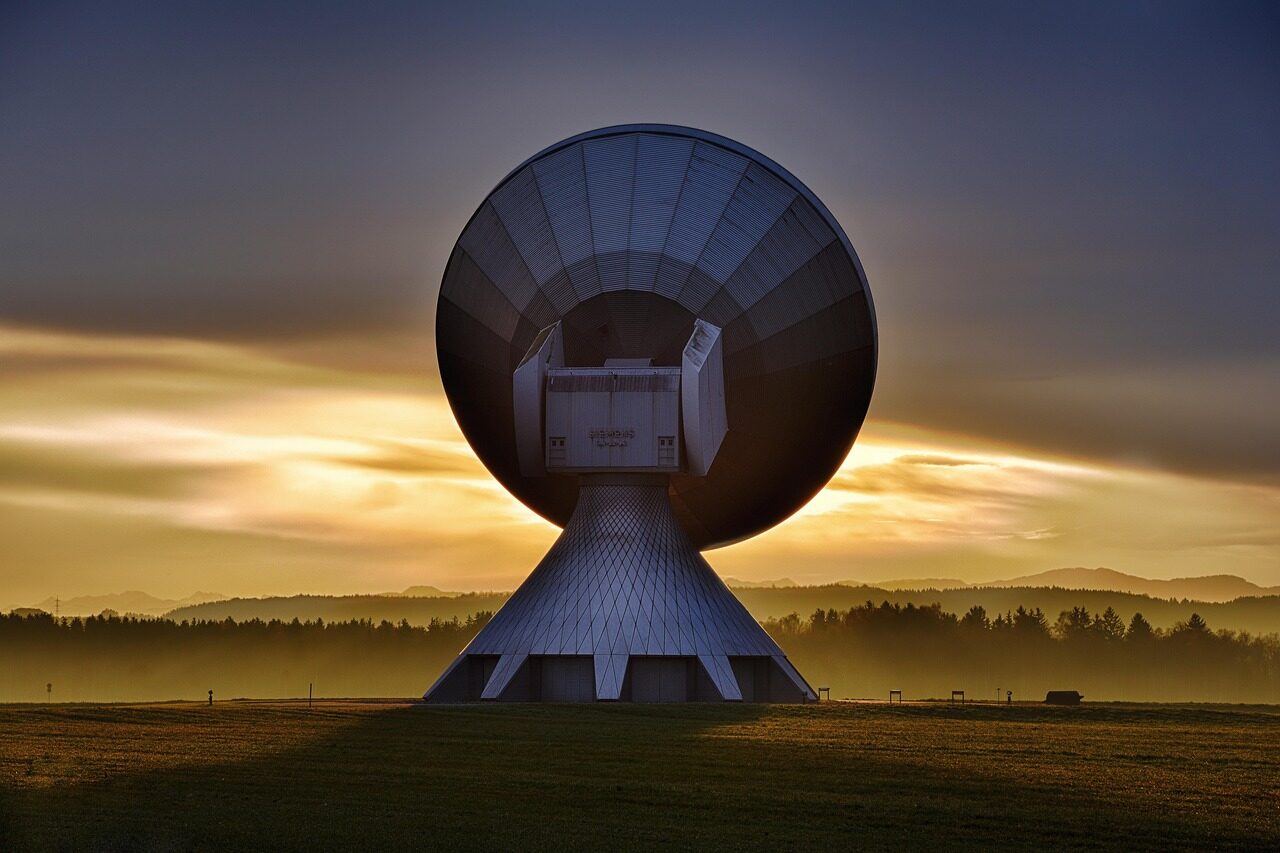 Large parabolic antenna at a ground station tracking a satellite across the sky.