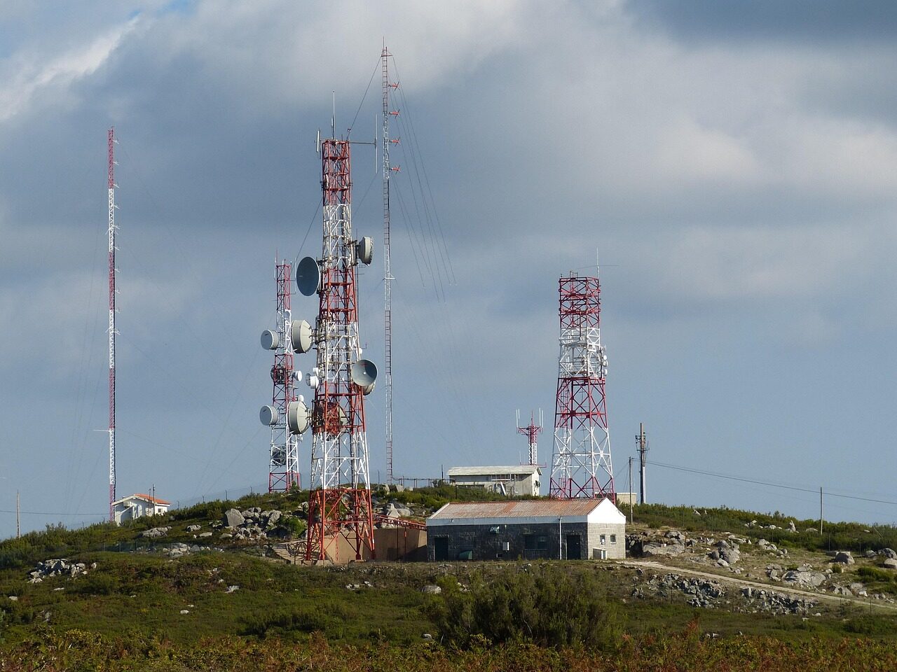 A soldier carrying a ruggedised radio node with antenna on patrol through open ground.